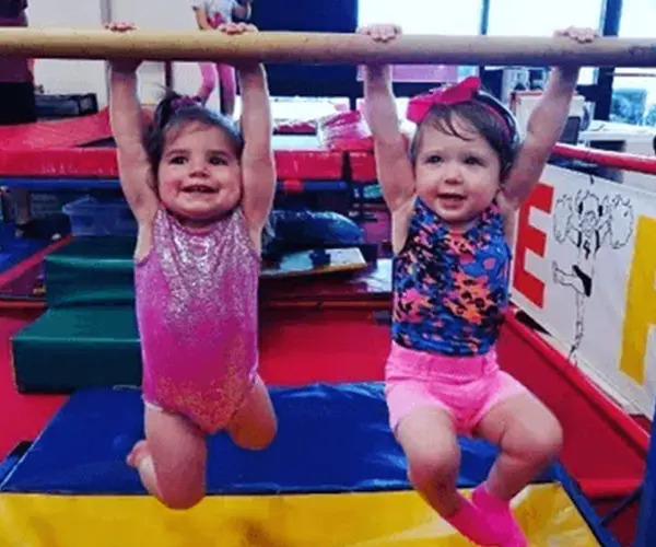 Two little girls hanging from a bar in an indoor gym.