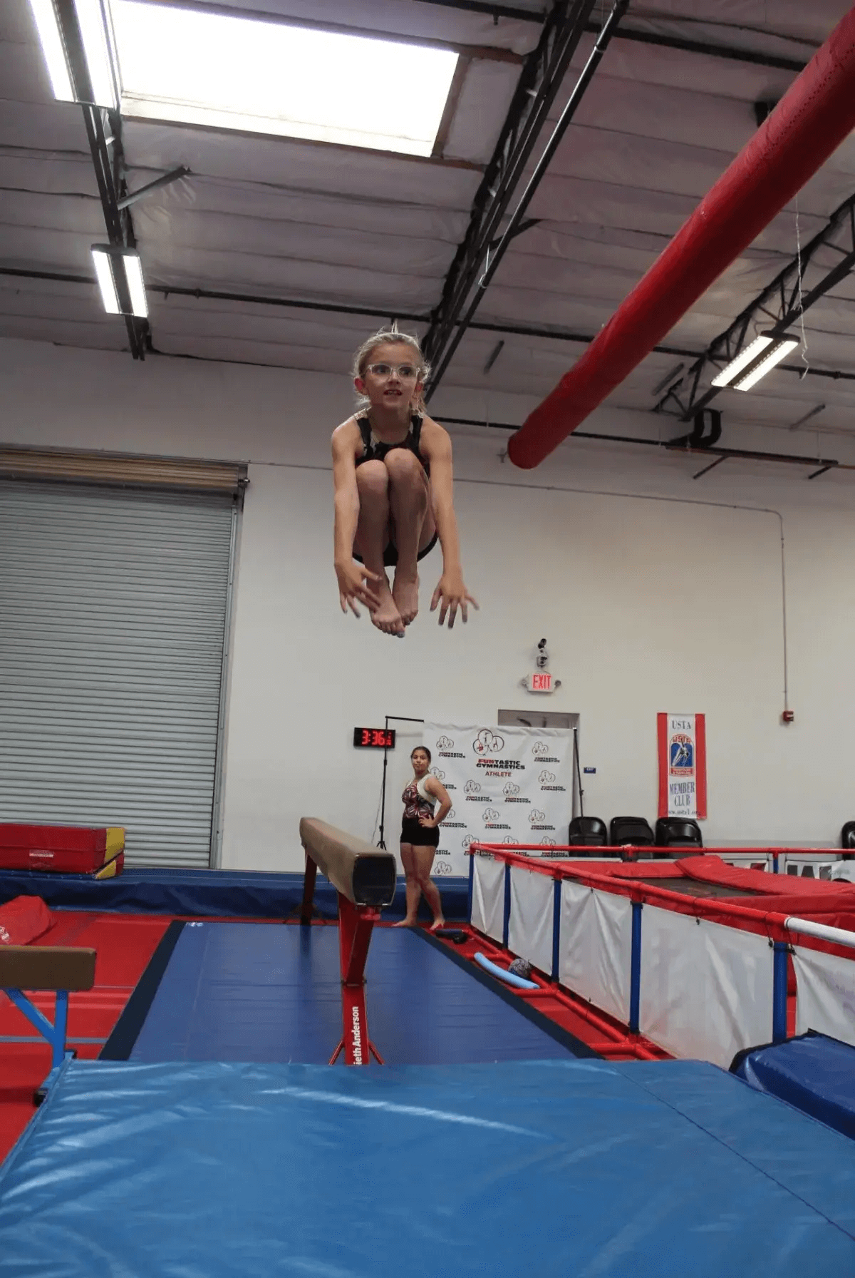 A girl jumping on a balance beam in an indoor gym.